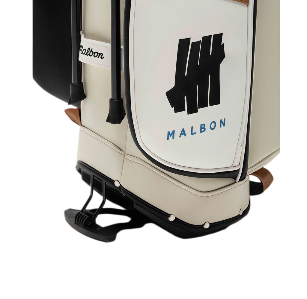 Bottom close-up of Malbon Golf bag showing protective rubber feet, embossed 'HH MALBON' logo on side panel, and reinforced base with brown leather accent trim.