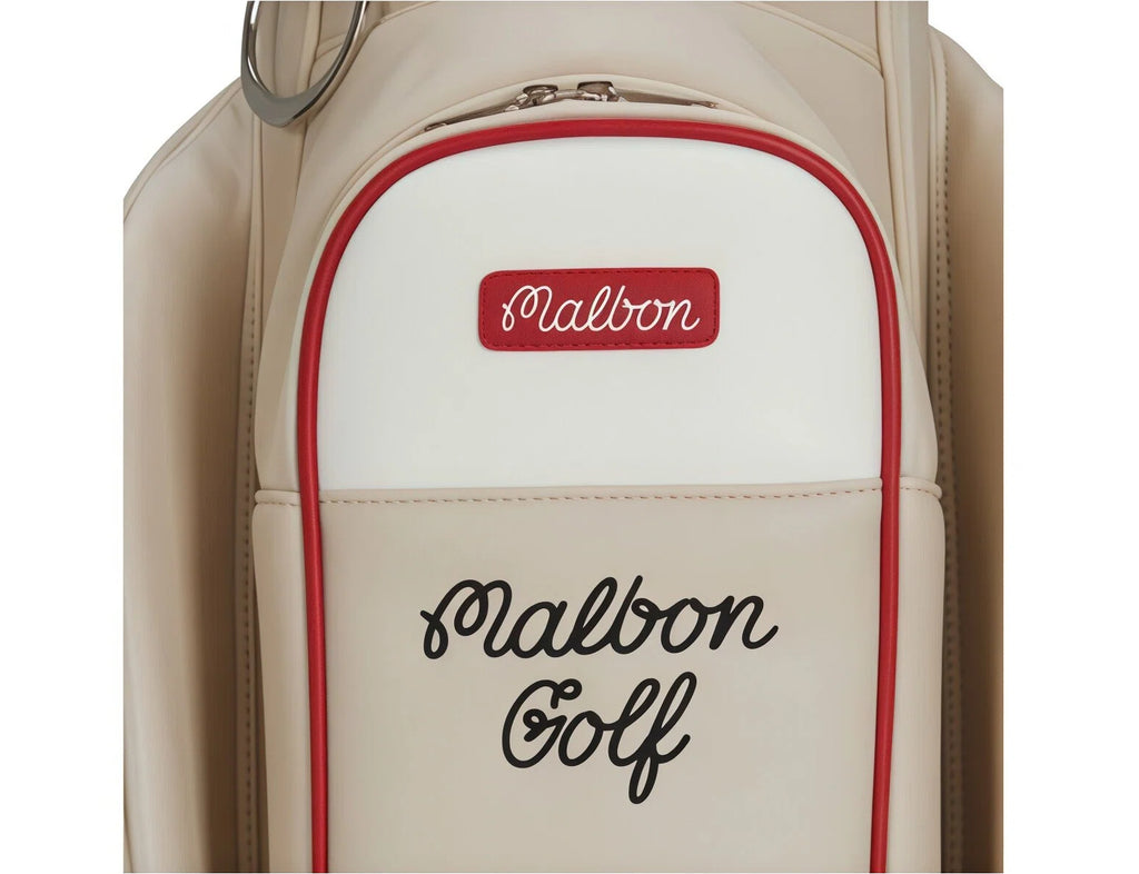 Top-down view of Malbon Golf bag back panel showing red "Malbon" patch and black cursive "Malbon Golf" text. Premium detailing with contrasting red trim for visual appeal.