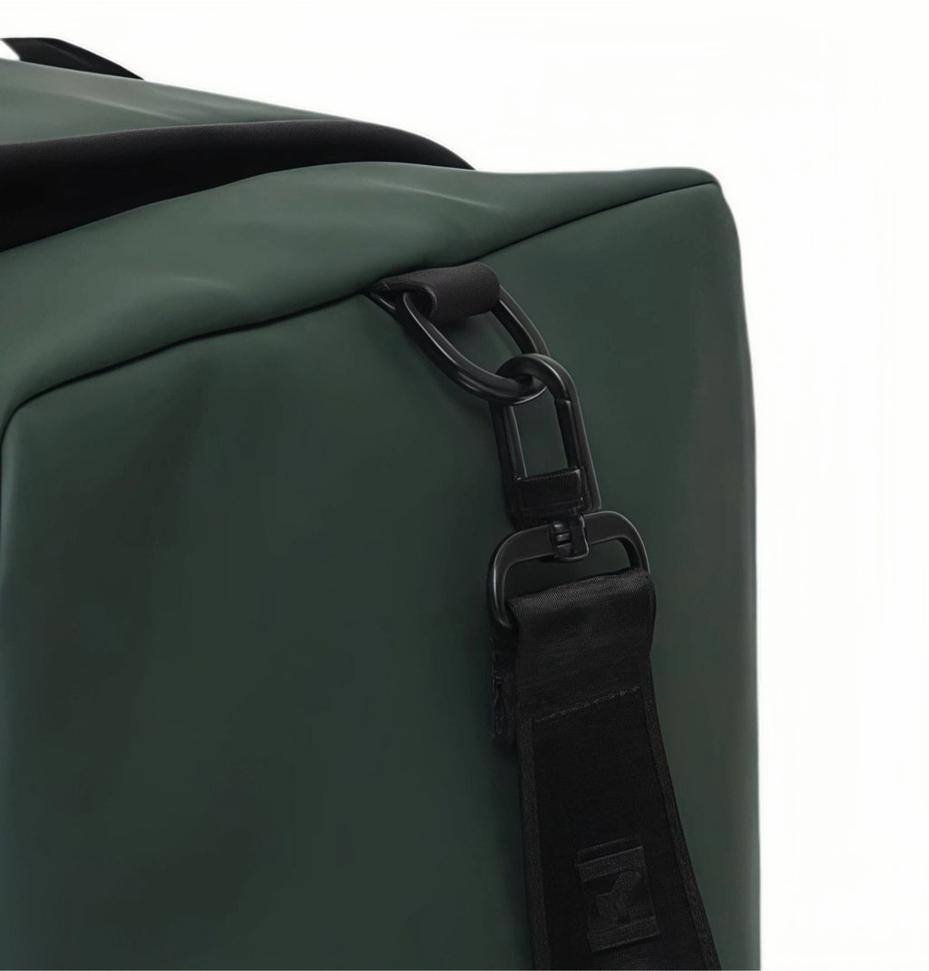 Detailed close-up of Malbon Golf duffle bag's side handle attachment showing reinforced black metal D-ring and durable webbing strap for secure carry