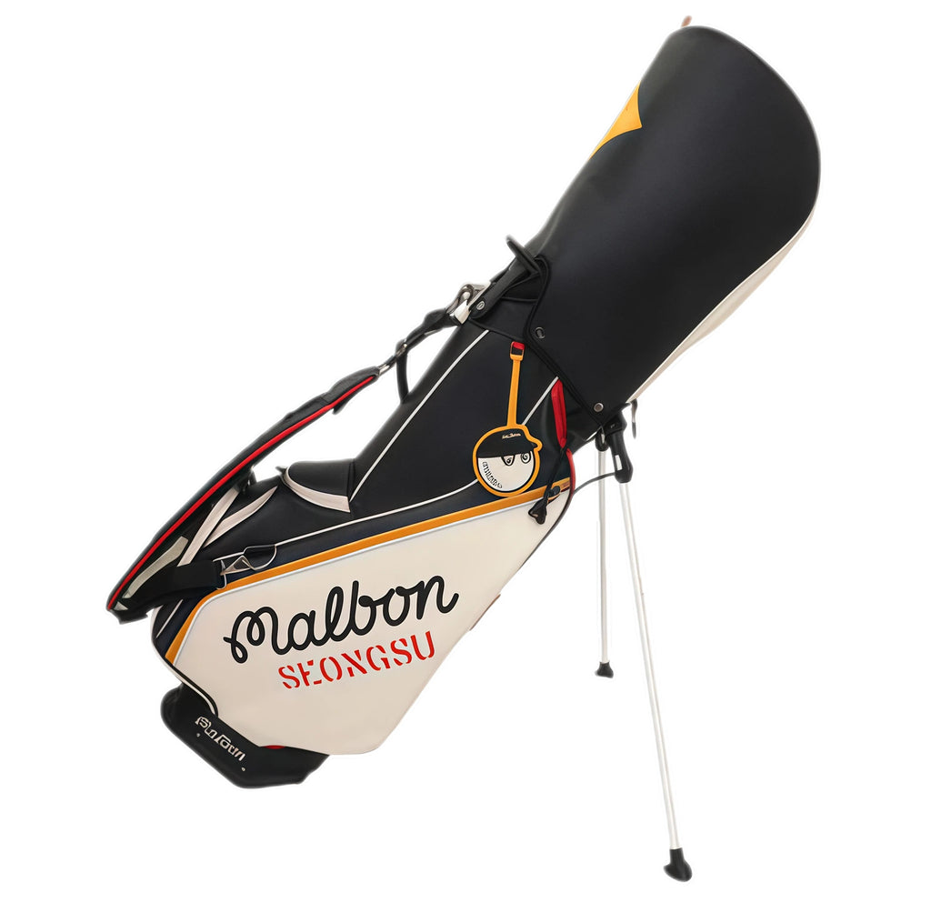 Angle view of Malbon Golf caddie bag with deployed stand legs, showing full stability and portability. Features include padded shoulder strap, internal compartments, and brand logo patch.