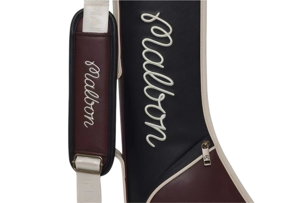 Close-up of Malbon Golf Classic Sunday bag showing burgundy shoulder strap with white "Malbon" script logo and beige fabric strap with metal hardware. Elegant design for stylish golfers.