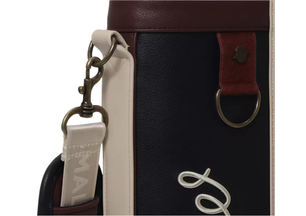 Top view of Malbon Golf Classic Sunday bag highlighting antique brass snap hook, leather-like loop, and branded zip puller. Premium craftsmanship and secure closure.