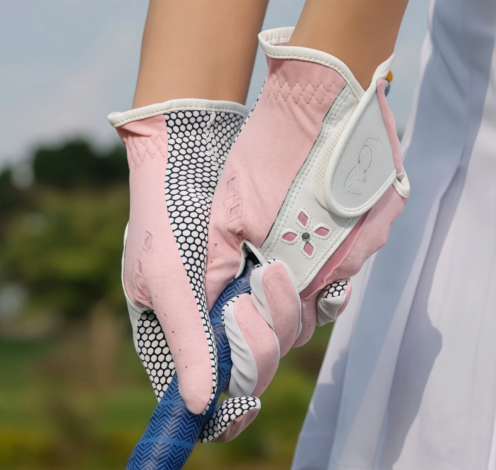 A close-up lifestyle shot of a woman wearing the pink PGM golf glove while gripping a golf club. The image demonstrates the glove's secure fit, breathable material, and the effective anti-slip grip on the club handle.