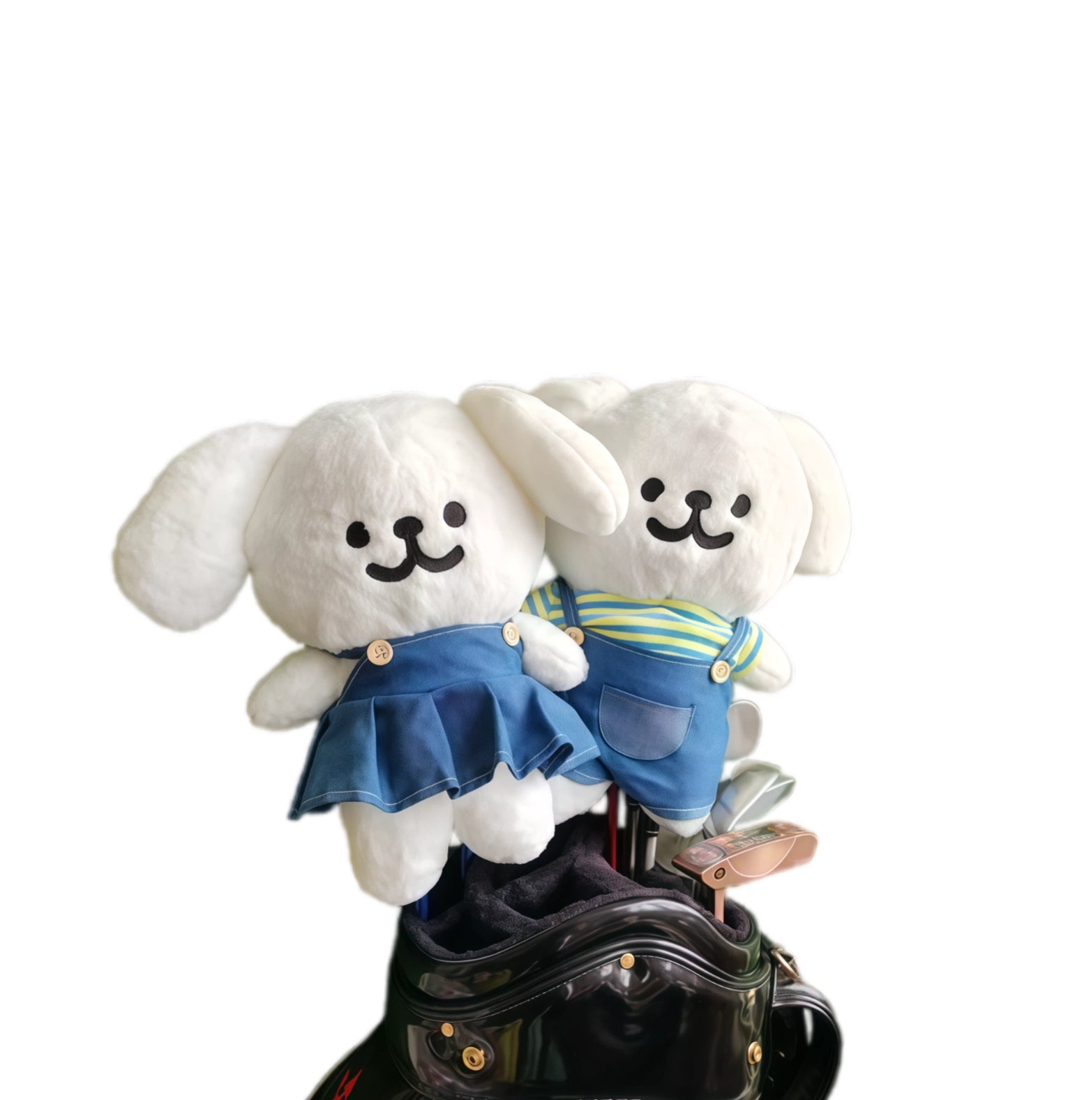 Two white plush toys with blue outfits sitting on a black handbag against a white background